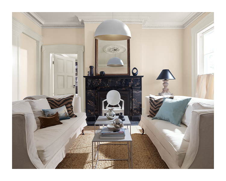 A light pink living room with matching white couches, pendant lighting, and a large fireplace built in navy and bronze marble.