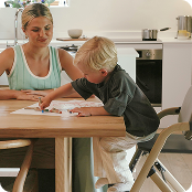 Image of Mother helping son who is drawing whilst sat in Nest & Nurture Highchair at kitchen table.