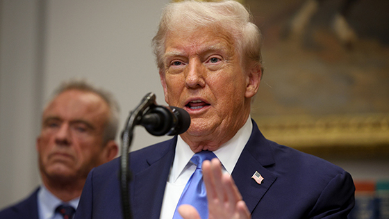 Donald Trump speaks from a podium with Robert F. Kennedy, Jr. looking on.
