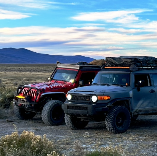 A Jeep Wrangler and a Toyota FJ Cruiser parked side-by-side on an open plain.