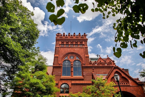 An exterior photo of the Fisher Fine Arts Library on a sunny day surrounded by tree greenery