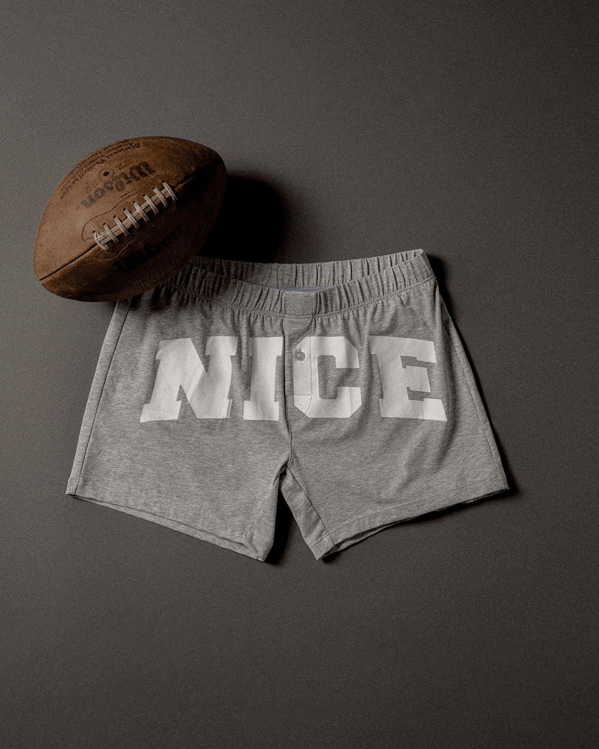 Pair of grey slim fit boxers with "NICE" on the front sitting next to a football 
