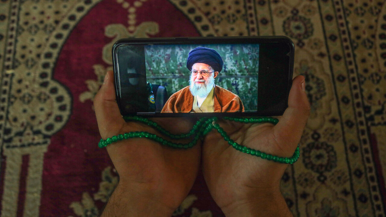 A Kashmiri Shiite Muslim man prays while holding a mobile phone displaying a portrait of Iran's Supreme Leader, Ayatollah Ali Khamenei