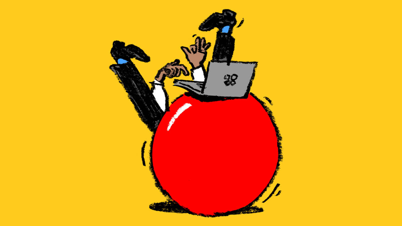 A person working on a laptop while boucing and falling from a big ball. 