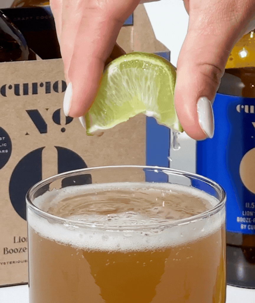 A lime wedge being squeezed into a glass of Curious Zero 