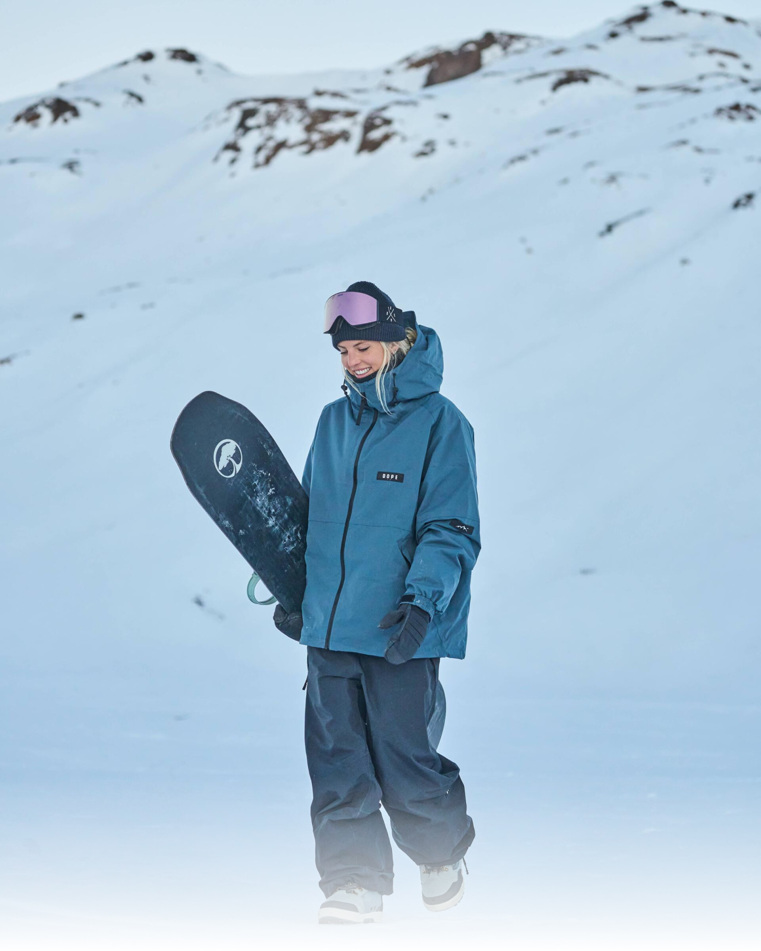 Barbara Perez smiling while walking down a snowy mountain with snowboard in hand