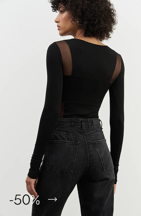 Astrid in The Eddit Top, a black long-sleeve top with sheer mesh panels on the back, styled with high-waisted black jeans.