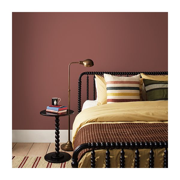 A bedroom with clay red walls, a black spindle-frame bed and side table, and cozy tan bedding with striped pillows.