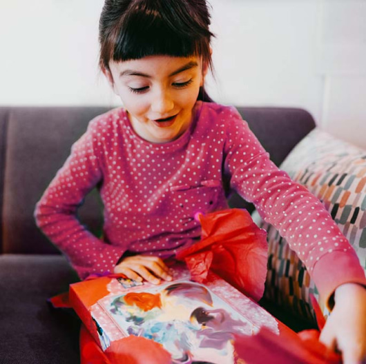 An excited little girl tears the wrapping paper off a present.