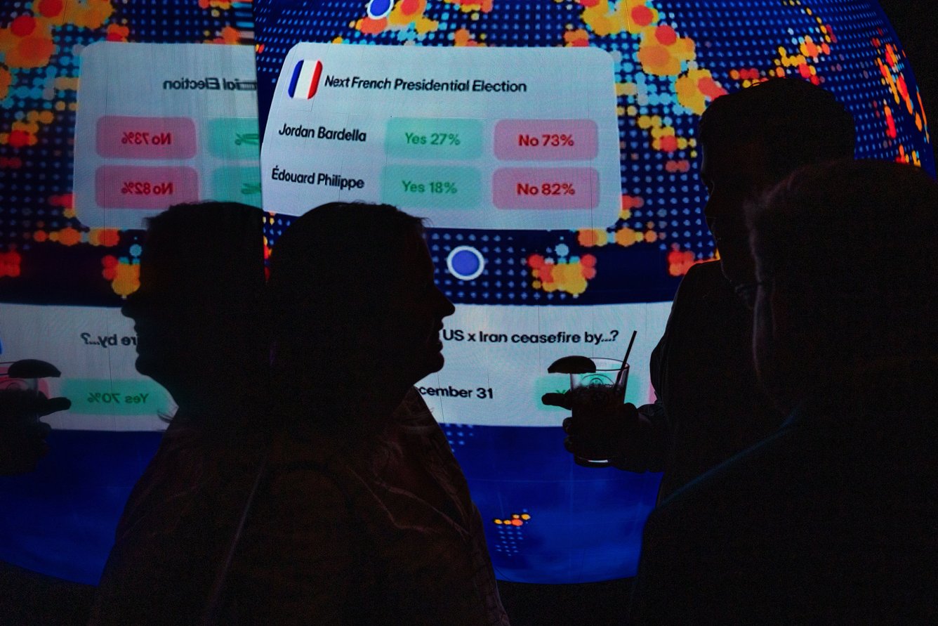 Silhouettes of guests against betting screen at Polymarket event