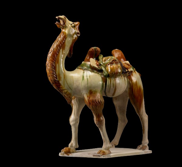 Ceramic figure of a camel carrying coiled silk and folded fabric. 