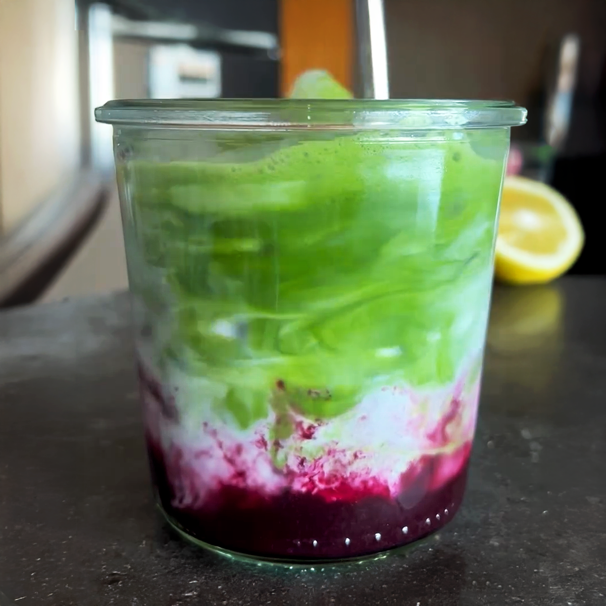 Iced matcha latte with blueberry syrup in glass on counter.