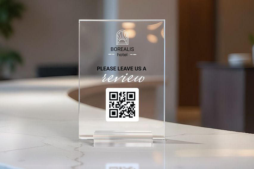 Clear acrylic tabletop sign with QR code requesting hotel guest reviews on a front desk