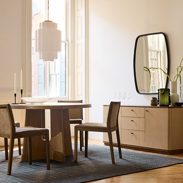 A modern dining room features a circular table with square-backed chairs, a large oblong mirror, and a matching sideboard.