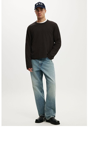 Male model wearing black long-sleeve crew neck sweatshirt, light blue jeans, and navy cap