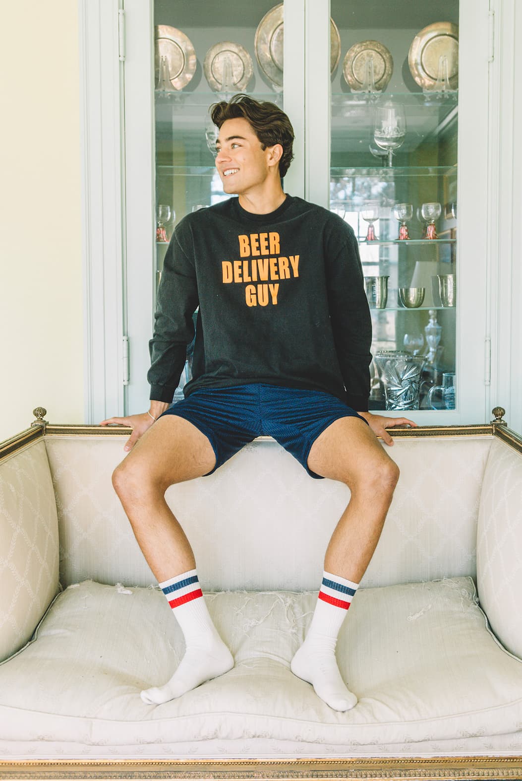 man sitting on a couch wearing blue lounge shorts, crew socks and a crew neck sweater