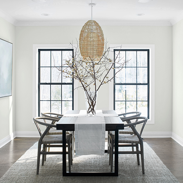 A serene dining room with off-white-painted walls, a light-gray ceiling and trim, black wood table and chairs, and wicker chandelier.