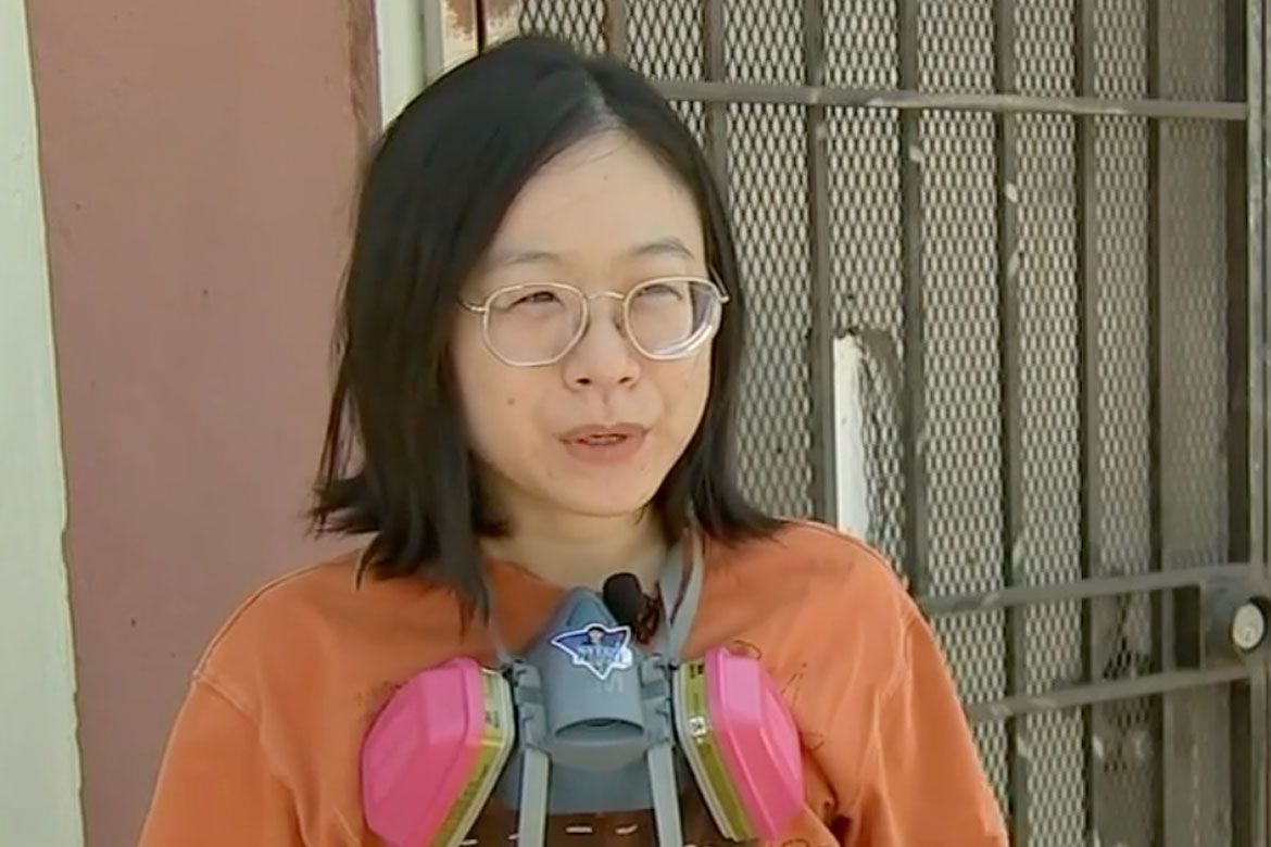 UCLA researcher Jing Li wearing glasses and an orange shirt, and with a pink and gray respirator mask around her neck.
