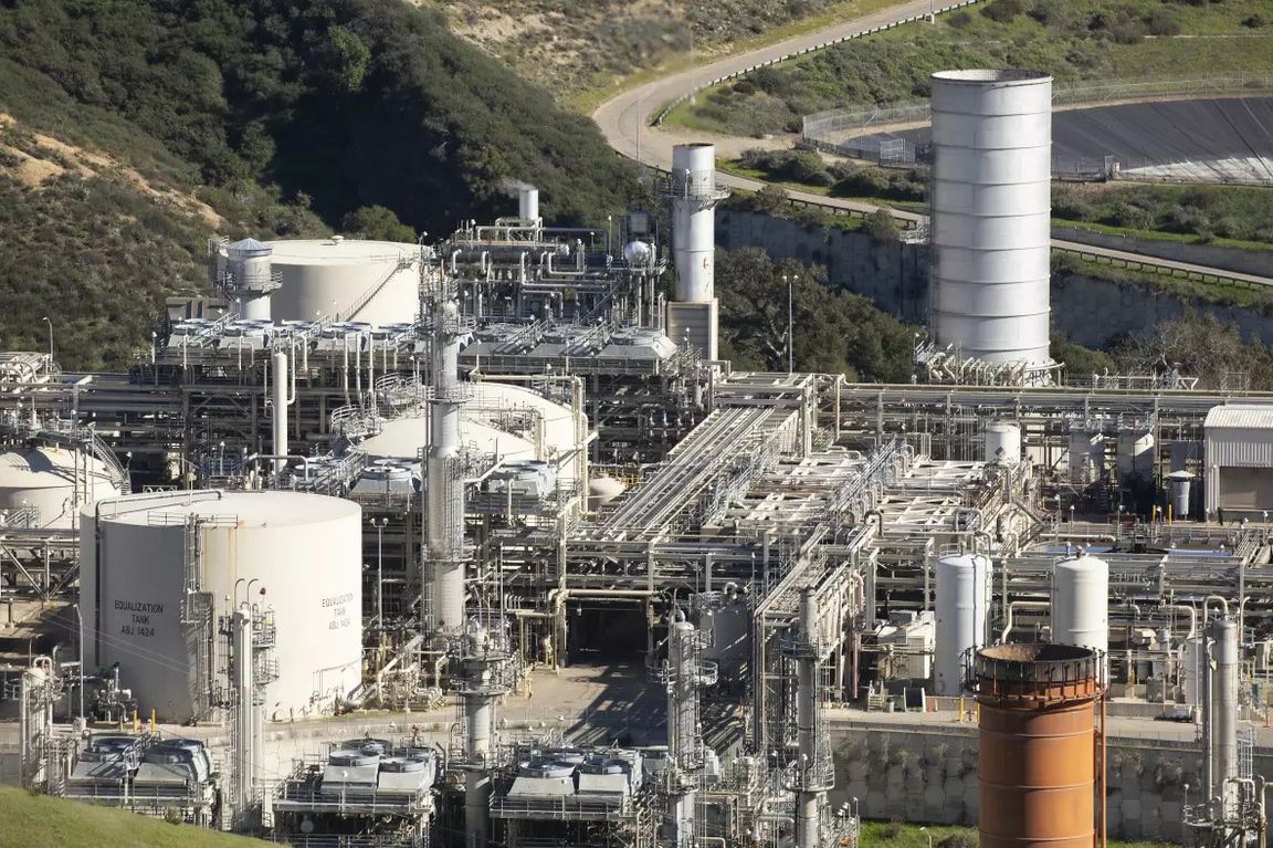 An industrial oil and gas processing facility with tanks, pipes and towers sits in a canyon in Goleta, California, surrounded by hillsides near the coast.