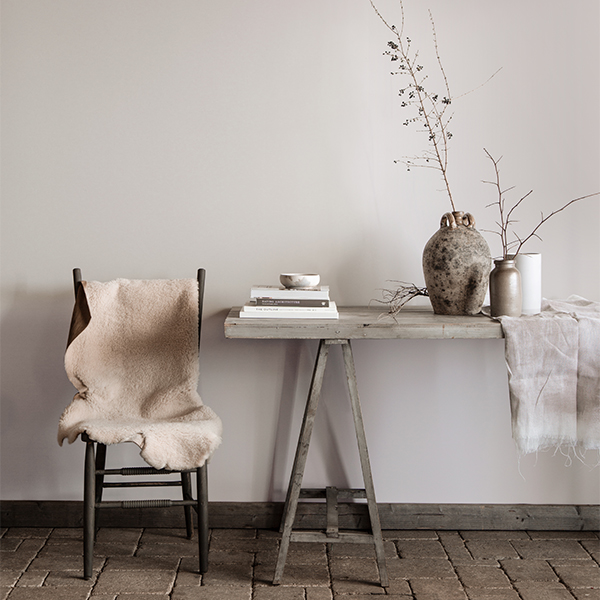 Gray dining area featuring a rustic table with books, vases, and branches, and chair topped with white fur blanket.