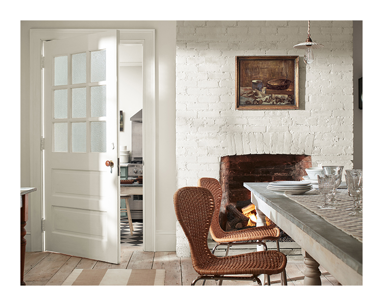 A white painted dining room houses a stone fireplace, a gray stone table, and brown woven chairs.